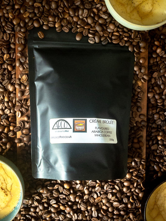 Bag of Arco Crème Brûlée-flavoured Arabica wholebean coffee on a bed of coffee beans, surrounded by ramekins of caramelised dessert, reflecting its smooth Brazilian roast infused with natural caramel and cream flavours