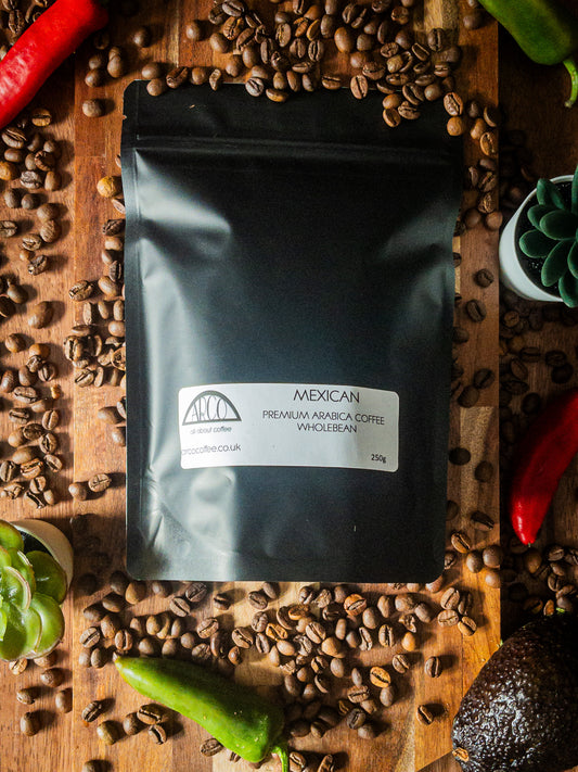 Bag of Arco Mexican premium Arabica wholebean coffee on a wooden surface, surrounded by coffee beans, avocados, and chillies, reflecting its smooth, mild flavour and high-altitude Altura origin